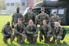A diverse group of IUPUI Army ROTC cadets on a field in front of a military helicopter.